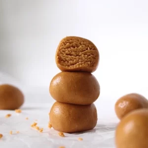 Dangerously delicious peanut butter protein bites are shaped into balls and stacked on top of one another. The top having a bite taken out of it to show the delectably soft texture inside.