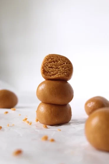 Dangerously delicious peanut butter protein bites are shaped into balls and stacked on top of one another. The top having a bite taken out of it to show the delectably soft texture inside.