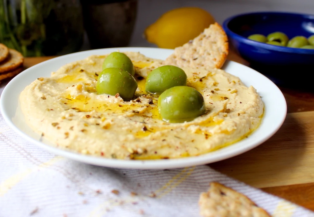 Beautiful Mediterranean Hummus, topped with bright green castelvetrano olives, and drizzled with olive oil.