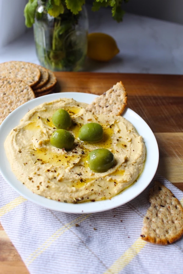 Beautiful Mediterranean Hummus, topped with bright green castelvetrano olives, and drizzled with olive oil.