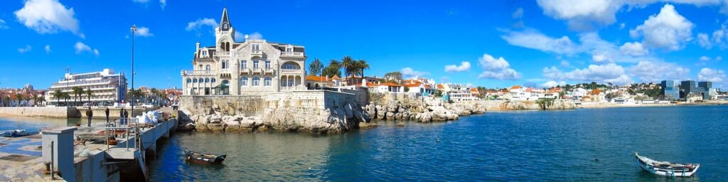 A view of Palácio Seixas, a symbol of the city of Cascais. The palace is overlooking the ocean, dotted with tiny fishing boats under a gorgeous blue sky.