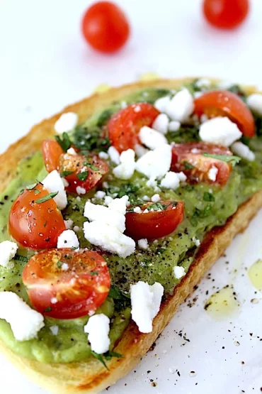 Spicy Avocado Toast with bright red, juicy, sliced tomatoes, white cotija cheese crumbles and spicy avocado spread onto a thick toasted slice of bread.