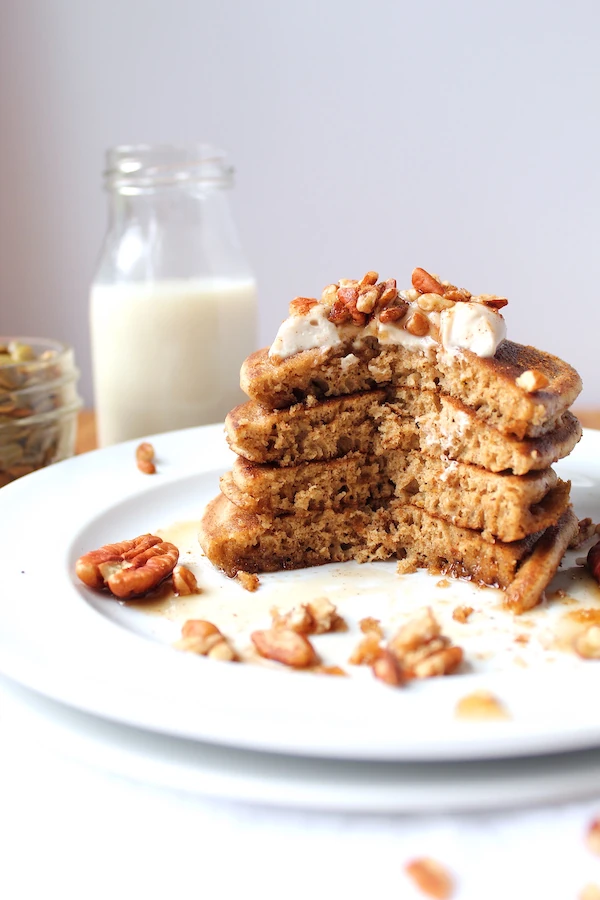 A glass of milk stands tall behind a stack recently sliced open showing the layers of these gorgeous pancakes.