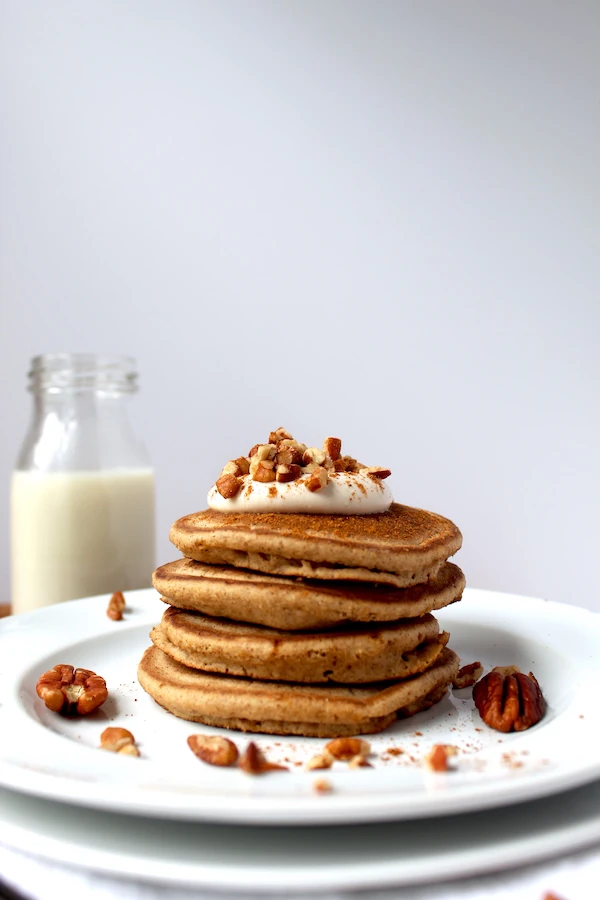 A gorgeous stack of pumpkin spiced pancakes topped with a pillow of vanilla yogurt, and garnished with crushed pecans.