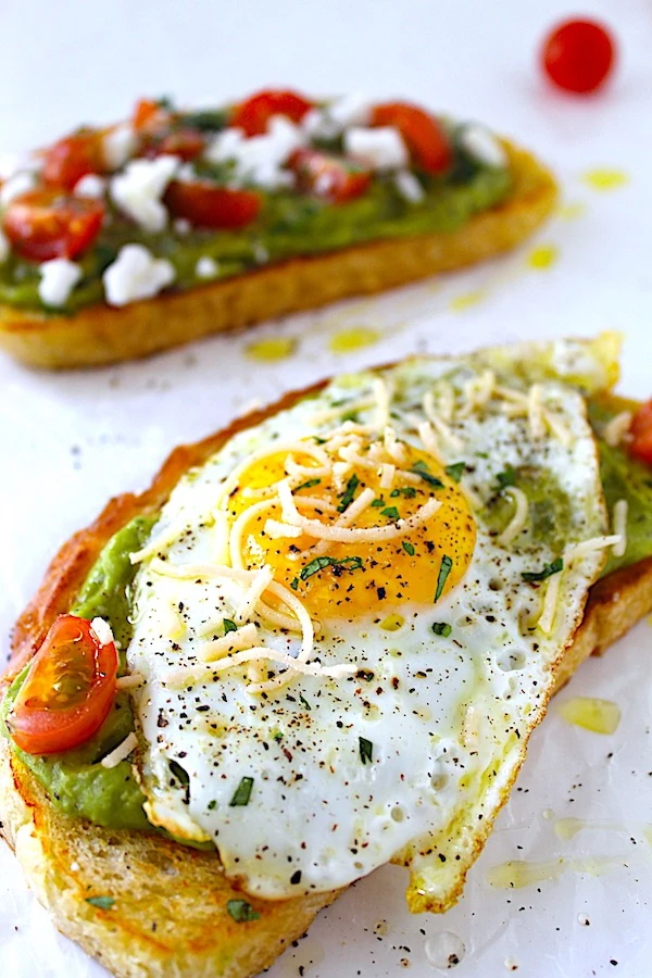 Gorgeous avocado toast covered with tomatoes, parmesan, parsley, and olive oil. Garnished with a elegantly cooked sunny-side-up egg!