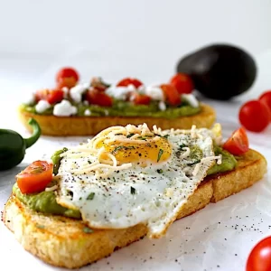 Spicy yet creamy avocado toast covered with tomatoes, parmesan, parsley, and olive oil. Garnished with an elegantly cooked sunny-side-up egg!