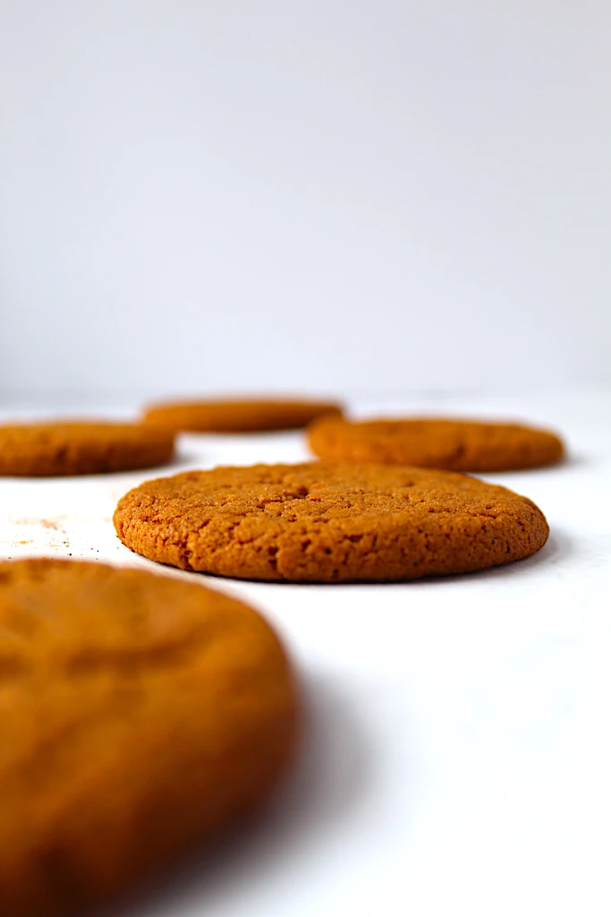 Multiple deep golden cinnamon colored molasses cookies with crinkly tops, lined across a cookie sheet.