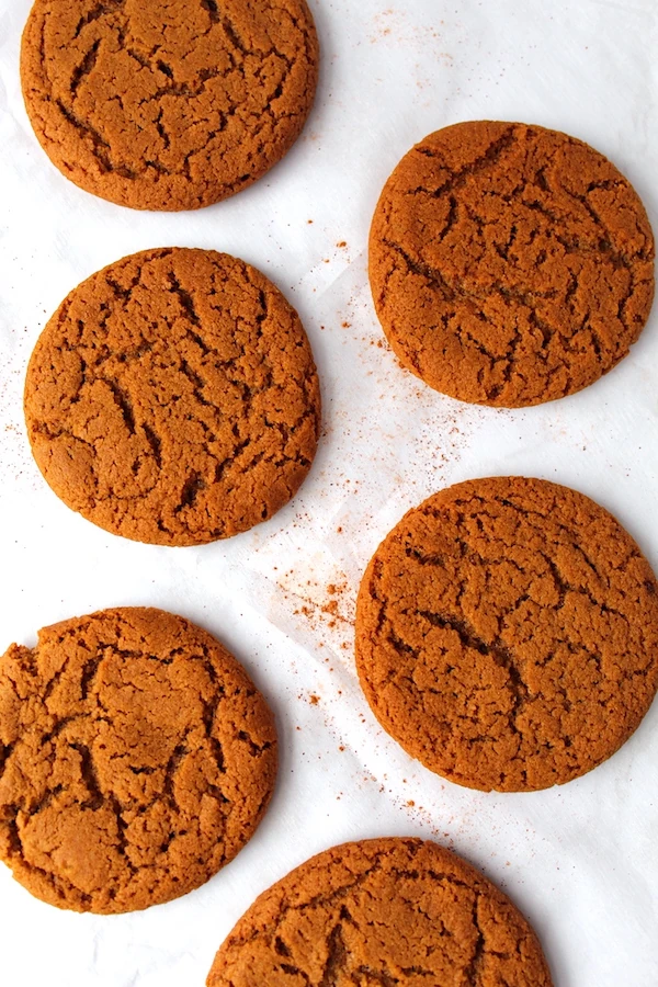 Cinnamon dusted ginger molasses cookies aligned onto a parchment covered cookie sheet.