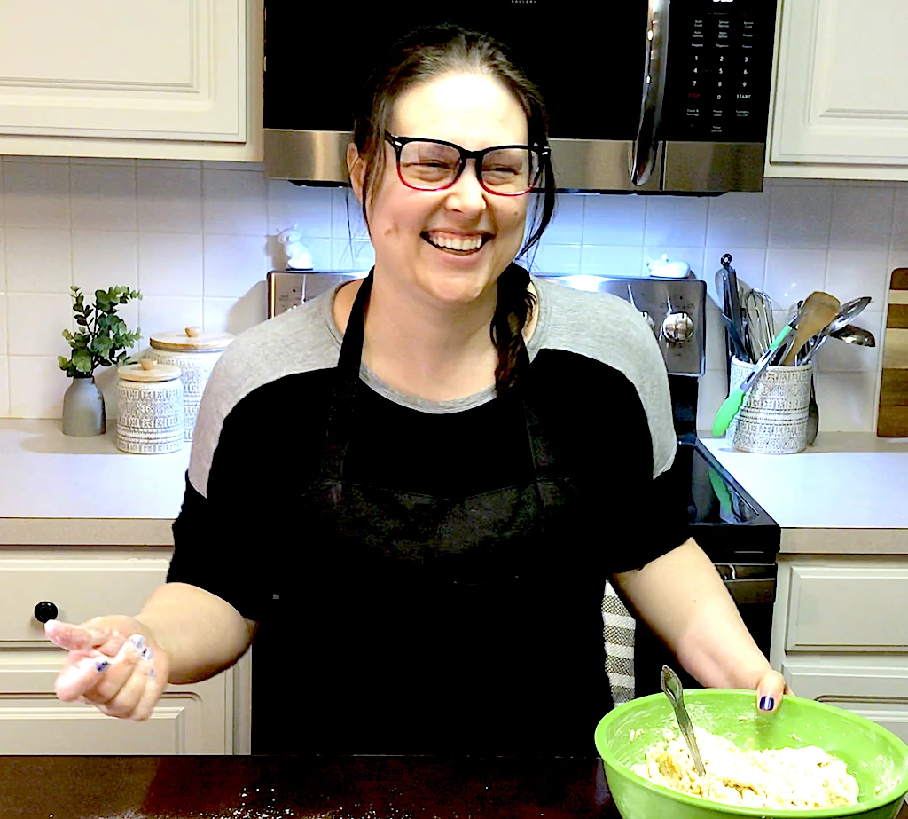 Brazelina laughing and cooking in the kitchen. She is making pizza dough, with flour on the table and a big smile.