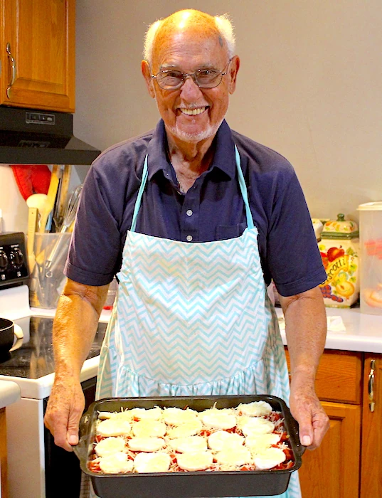 My Grampy (Milton), wearing an ear-to-ear-grin and my mom's apron. He's holding a tray of delicious food that he's proudly whipped up for the family.