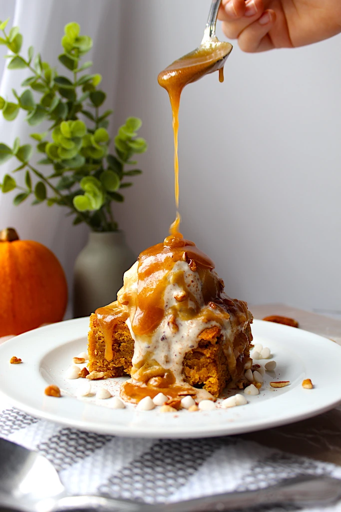 Warm maple-butter sauce dripping onto vanilla ice cream and chopped pecans.