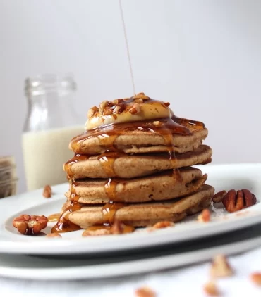 Light and Fluffy Pumpkin Spice Pancakes, drowned in maple syrup, topped with a pillow of vanilla yogurt, and garnished with crushed pecans.