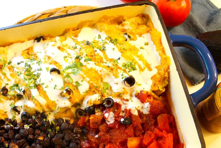 Enchiladas in blue dish covered with melted cheese, crema, cilantro, black beans and diced red tomoatoes.