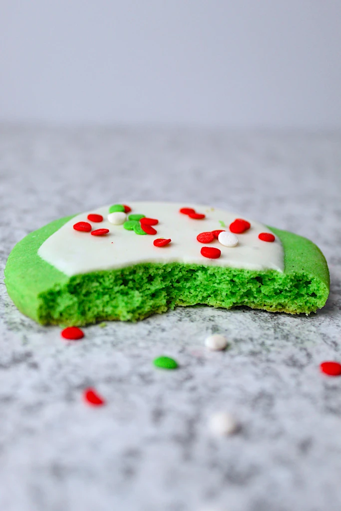 The inside of a sprinkles covered, bright green Grinch Inspired Almond Sugar Cookies and frosty white royal icing is shown.