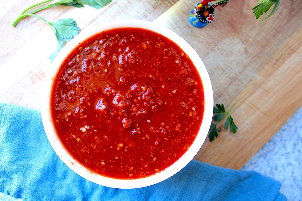 A rich, deep red hue is shown from the marinade in a bright white bowl. Fresh herbs and a Portuguese rooster surround the marinade.