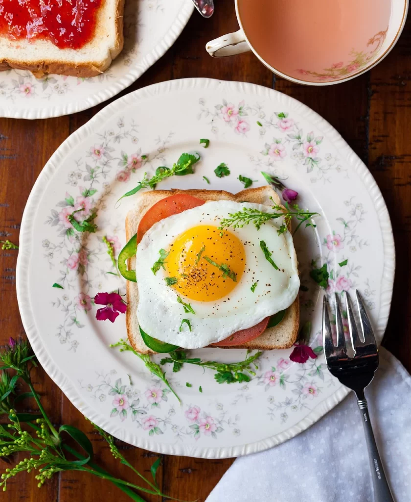 A brilliant breakfast spread is show. Eggs on a toasted sandwich are front and center. You can also see bread and jam and a cup of roasted coffee. Having breakfast for dinner can save money on groceries.