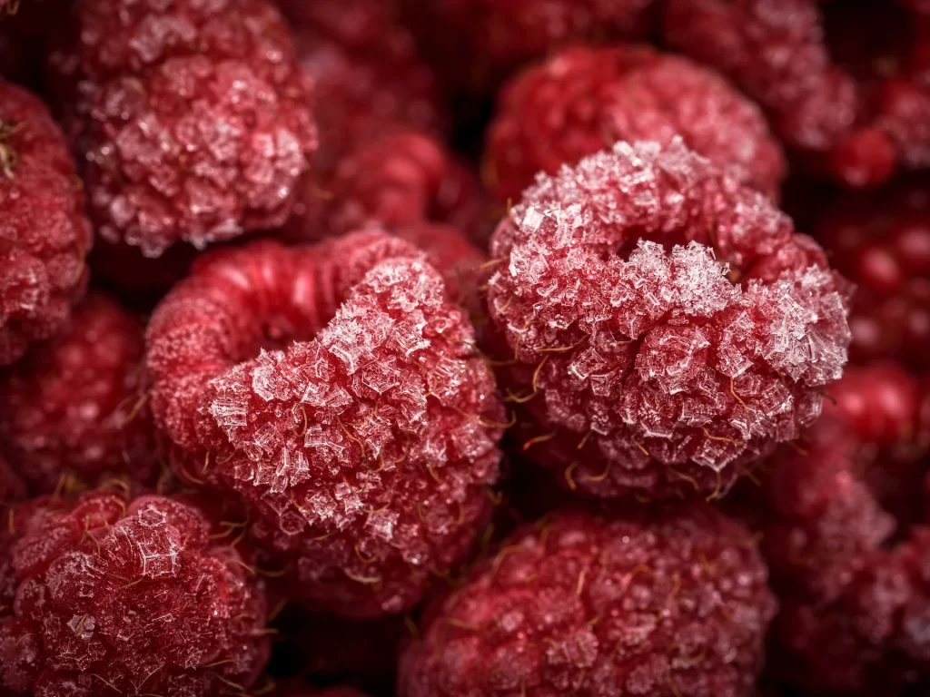 A close-up of deep red frozen raspberries are shown. Using frozen raspberries can help you save money on groceries.