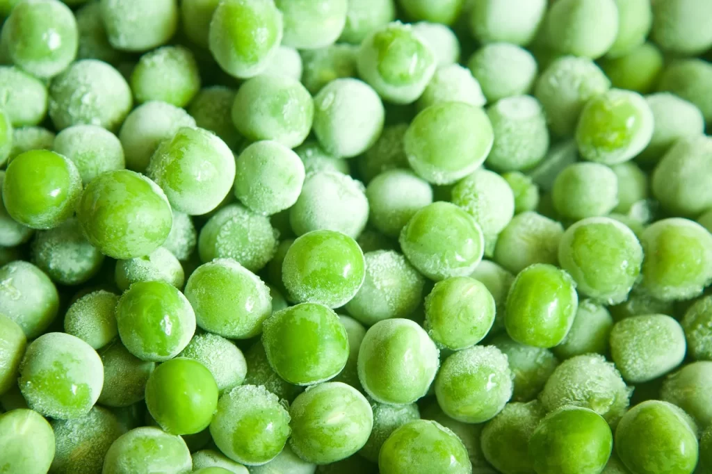 A close-up of frozen bright green peas are shown. Purchasing frozen produce is a great way to help you Save Money on Groceries.