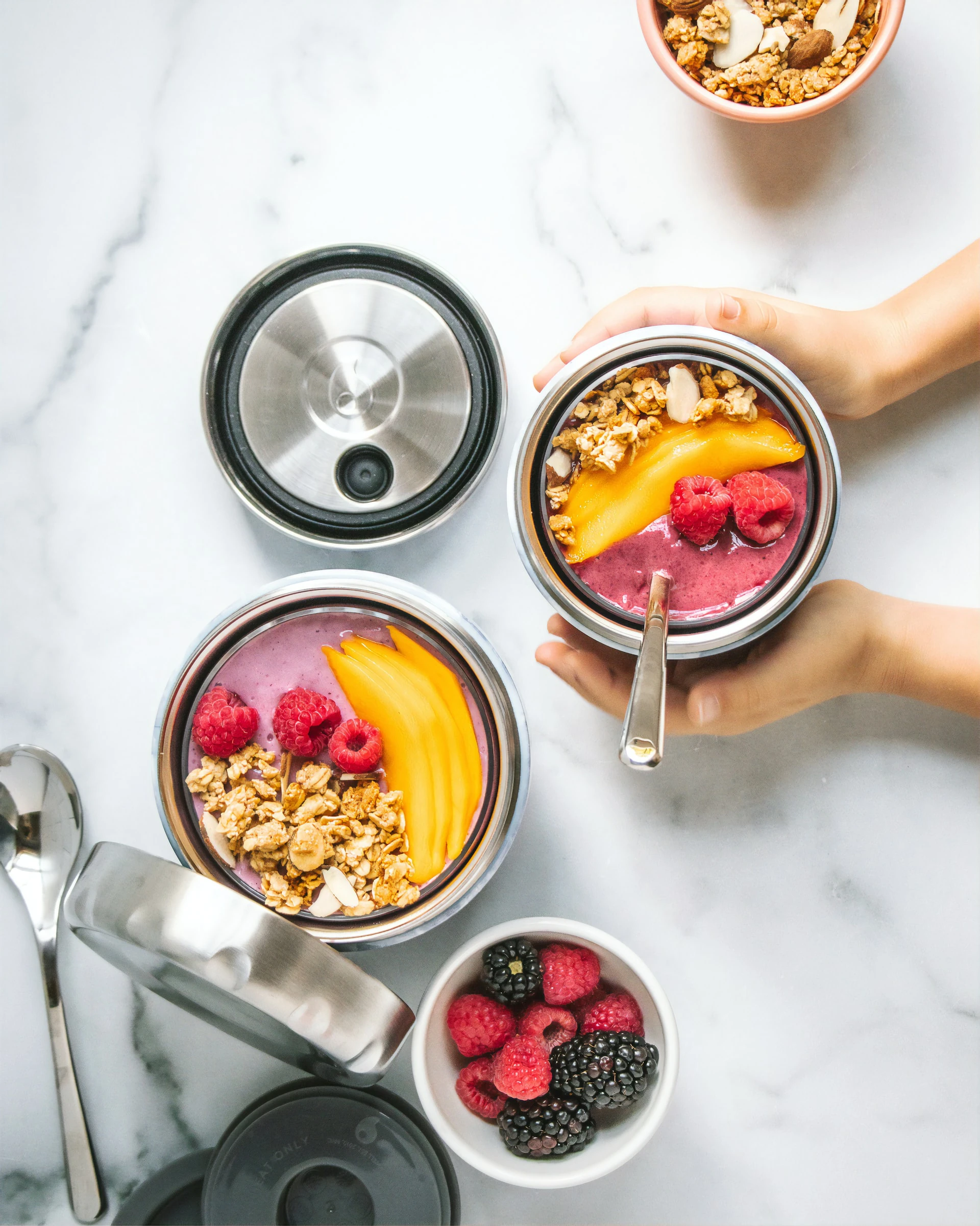 A woman is holding a mango, raspberry and granola smoothie bowl that has been proportioned into a jar.