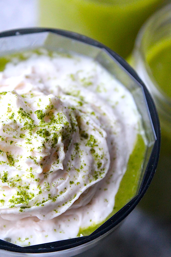 A close-up of almond whipped cream crowning a vibrant, healthy, green smoothie.