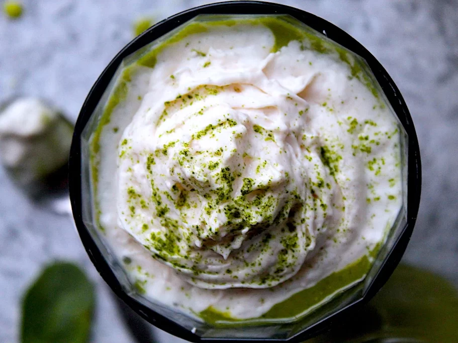 A close-up of almond whipped cream crowning a vibrant, healthy, green smoothie.