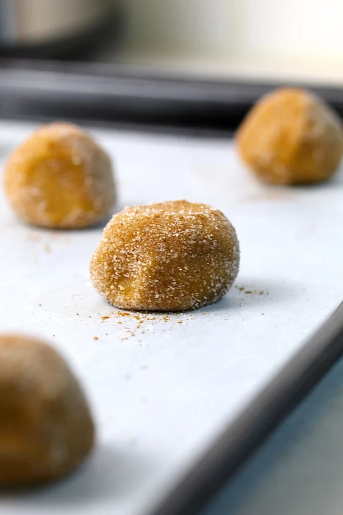 Unbaked cookie dough, dipped in pumpkin spice and ground ginger has been spaced on a parchment covered baking sheet ready for the oven.