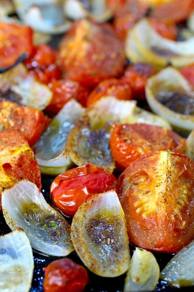 Roasted bright red tomatoes and white onions are peppered with fresh herbs and spices, fresh out of the oven.